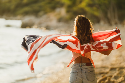 Rear view of a woman with US national flag enjoying a relaxing day on the beach.
