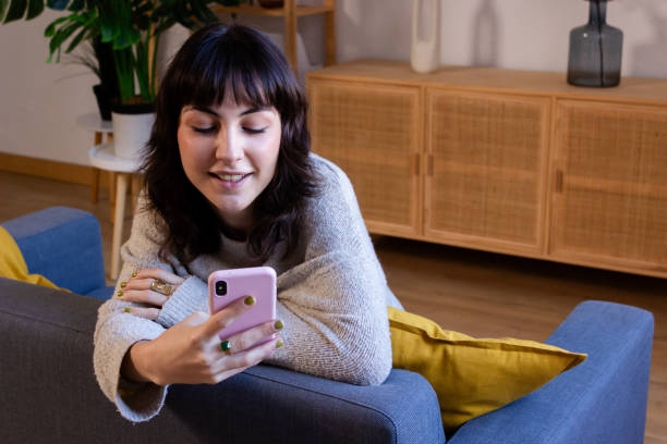 istock Young woman using mobile phone while sitting on sofa in living room at home 1831091079