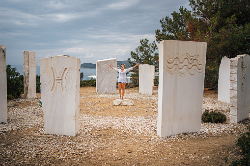 Young cheerful woman in the middle of the zodiac signs arranged in a circle near the Metalia Beach, Limenaria, Thassos, Greece