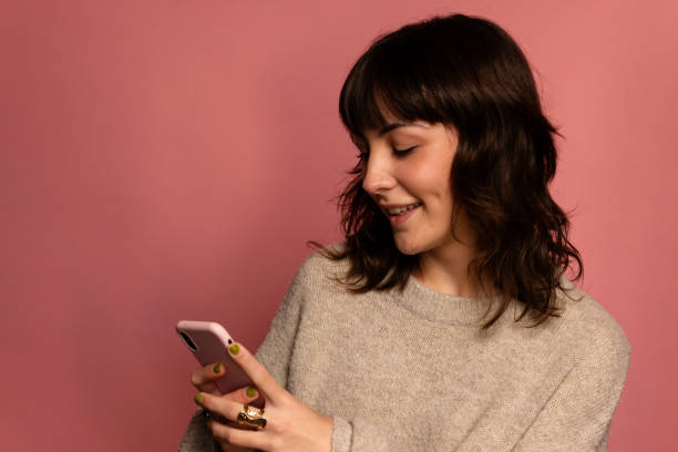 istock Smiling young woman using her mobile phone on a pink background. 1831094382