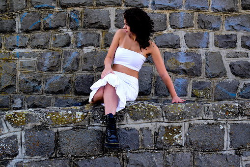 Young woman in fashionable dress poses against brick wall.