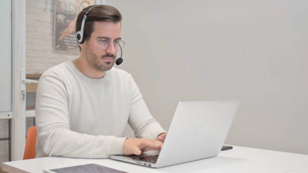 istock Young Man with Headset Working on Laptop in Call Center 1831104954