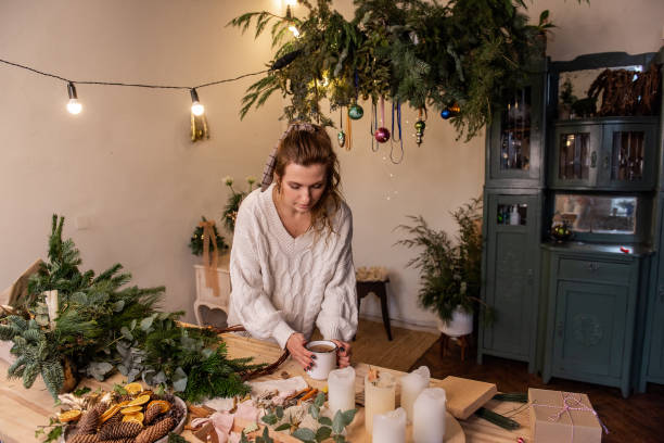 istock Young woman florist workshop makes Christmas wreath, drinks hot tea from white cup 1831117115