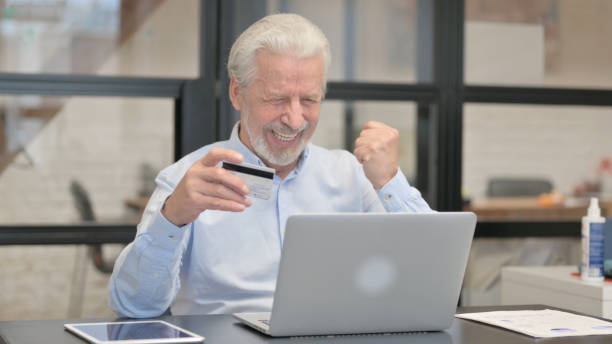 viejo hombre de negocios que disfruta de las compras en línea en la computadora portátil en la oficina - 32557 fotografías e imágenes de stock