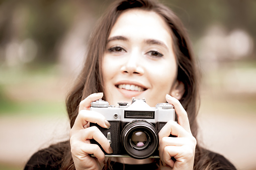 Beautiful young woman photographer taking picture outdoors with an analog camera.