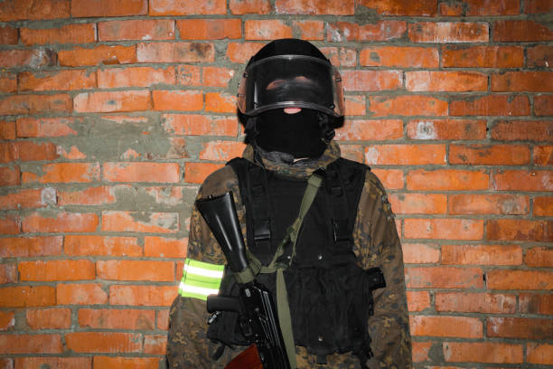 Studio portrait of a male soldier with a rifle wearing a helmet, he is standing against black background.