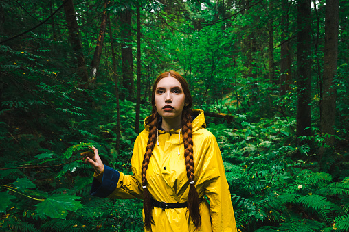 Woman in a yellow raincoat walk her way through a green wet forest during the rain. The concept of travel and tourism.