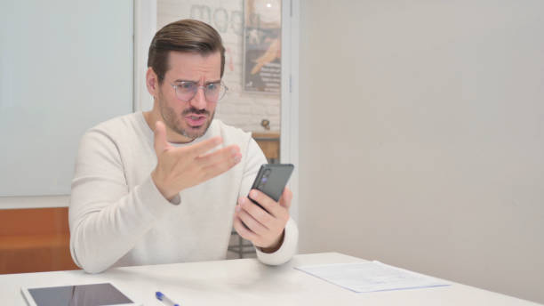 istock Middle Aged Man Shocked by Loss on Phone in Office 1831174475