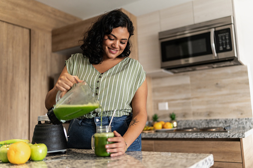 Young woman preparing detox juice in kitchen at home