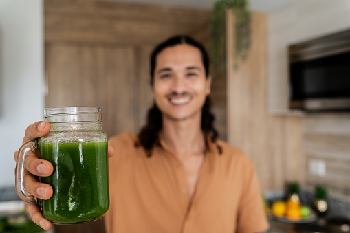 Close-up of man holding a glass of detox juice in kitchen at home