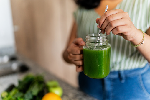 Close-up of woman holding a detox juice and mixing it at home