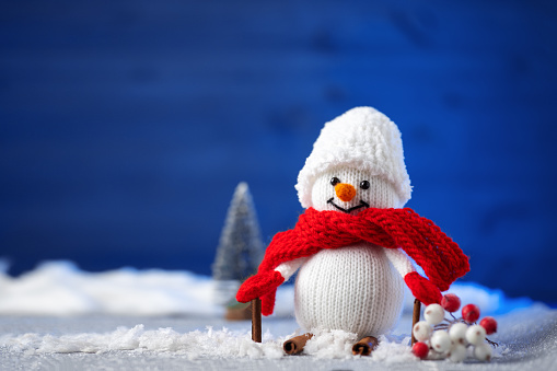 Knitted Toy New Year's snowman is skiing in the snow. Blue background, copy space