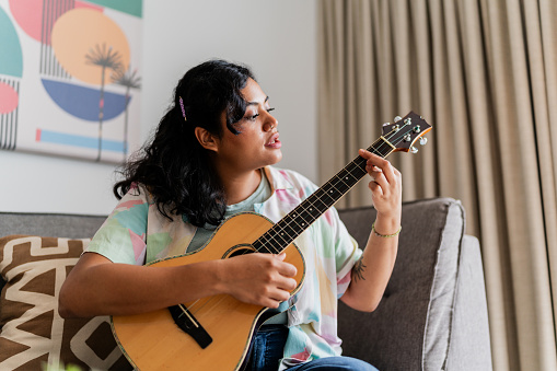 Young woman playing guitar and sing in living room at home