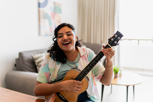 Portrait of a happy young woman playing guitar at home