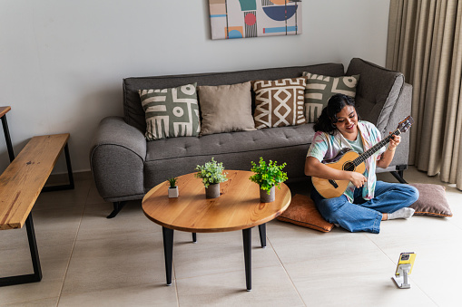Young woman doing a live stream playing guitar in living room at house