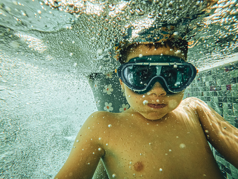 Young boy swimming underwater in the swimming pool.