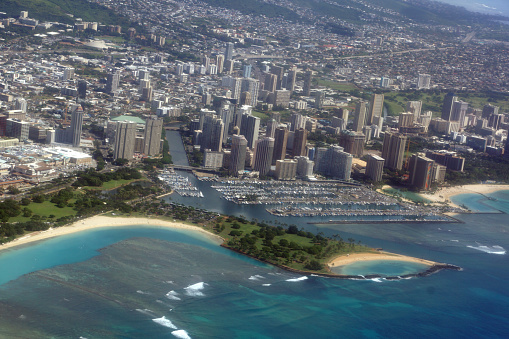 Honolulu - November 10, 2014:  Aerial view of Honolulu, Hawaii, showing the coastline and the city. The photo includes Magic Island, Ala Moana Beach Park, Ala Wai Harbor and Waikiki, which are popular attractions for tourists and locals alike. The photo shows the contrast between the blue ocean and the white beach, and the urban landscape and the green mountains. The photo is taken from a high angle, capturing the vastness and beauty of the island.