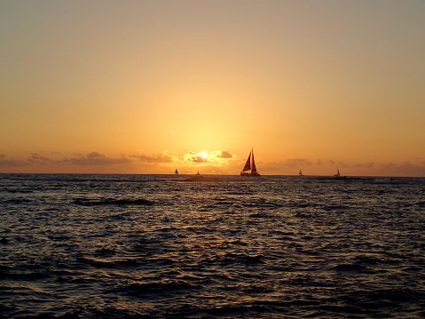 A beautiful view of the sunset over the ocean in Waikiki, Hawaii, with sailboats on the water.