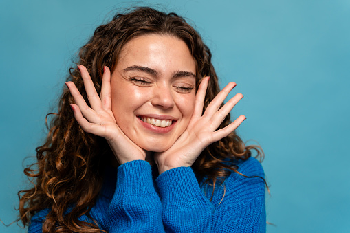 Happy young woman with long curly hair in blue sweater on blue background