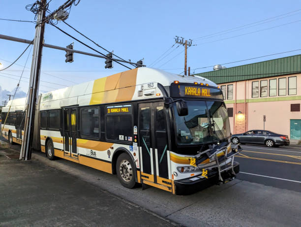 Honolulu - November 3, 2022: Honolulu city bus parked on the side of the street with a green building in the background. The bus is a New Flyer Xcelsior model with a bike rack on the front and a destination sign that reads \