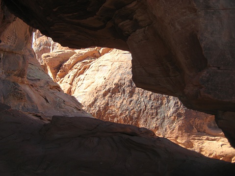 The textures and color of a beautiful rock wall are visible as the sun hits it, as seen from inside a small cave in the rocks.