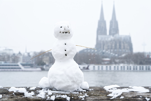 a little snowman on the wooden railing of the rheinboulevard with the cathedral in the background during a rare snowfall at the beginning of december 2023 in cologne