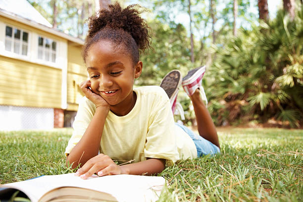 istock Happy African American girl reading book while lying on lawn 183137886