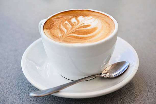 cup of latte coffee and spoon on gray counter - 茶碟 個照片及圖片檔