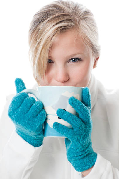 Pretty blond drinking hot chocolate or coffee from a mug wearing a white fleece pullover and teal gloves.Similar images: