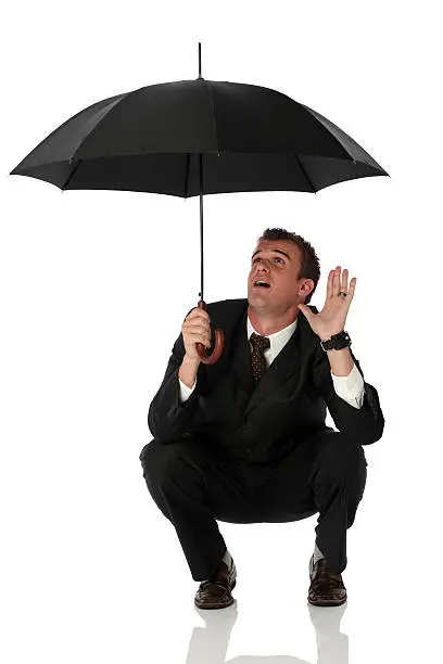 Photo of Businessman crouching under umbrella