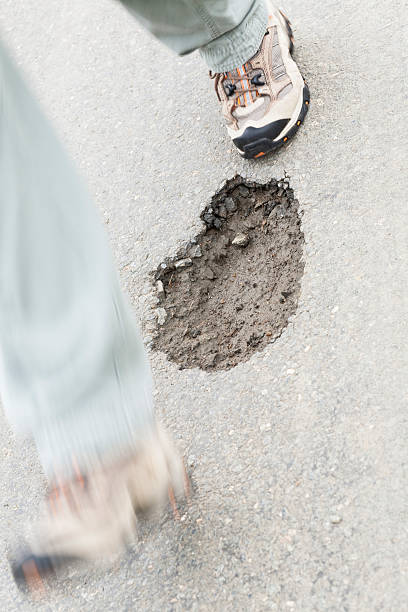 istock Stepping over a pot hole hazard in road 183142462