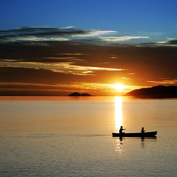 XL canoe sunset father and son in silhouette conoeing at sunset, square frame (XL) great lakes photos stock pictures, royalty-free photos & images