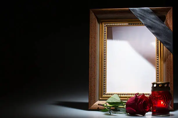 frame with black ribbon, red rose and cemetery candle in front of dark background