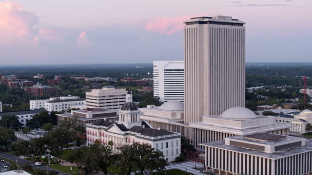 New and old State Capitol in Greek Revival under purple twilight sky in Downtown Tallahassee, Florida. Aerial footage with wide panning-orbiting camera motion.