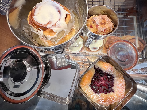 Ethical consumerism - sustainable stainless steel containers on a display counter brought in by the customer to reduce packaging waste for takeaway baked goods (cinnamon bun, cranberry white chocolate scone, blueberry danish) at a bakery.  Vancouver, British Columbia, Canada.
