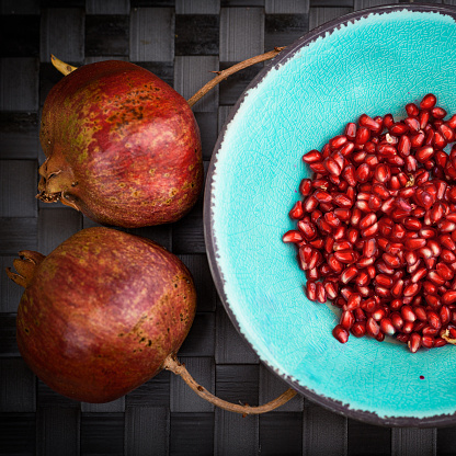 Deliciously Crisp, pomegranate seeds in turquoise bowl & fruits, against dark background, fresh and juicy.