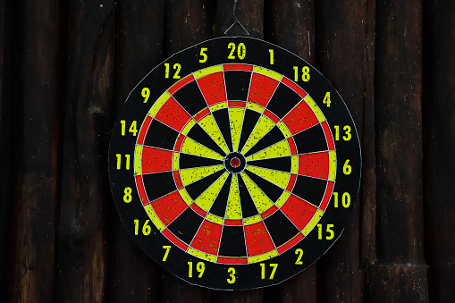 Dartboard which has a lot of holes on the surface after pull the arrows out and hanging on the wooden wall.