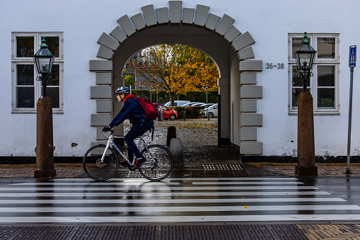 Odense, Denmark Oct 30, 2023 A man bikes by an archway and over a crosswalk in the old town.
