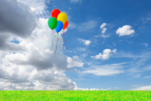 Bunch of five multicolored balloons floating in the blue sky over the green hill with copy space.