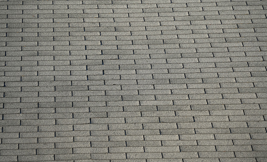 Roofer builder worker finishing folding gutter. He is up a ladder, photo taken from ground looking up, low angle view. He wears a tool belt, sky and clouds