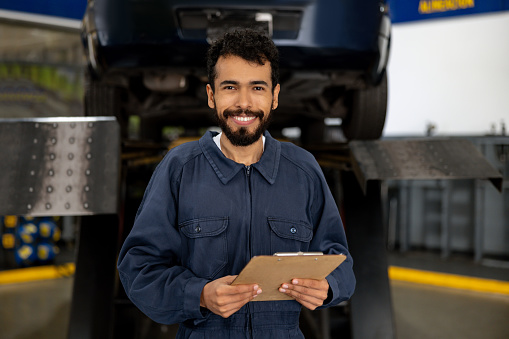 Portrait of a happy Latin American mechanic working at an auto repair shop and looking at the camera smiling