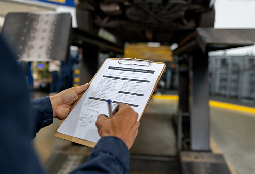 Close-up on a mechanic making a diagnosis on a car at a garage and writing on a form using a clipboard