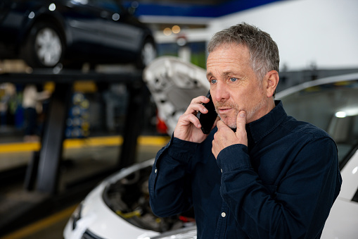 Latin American man looking worried taking on the phone at the mechanic after having a vehicle breakdown