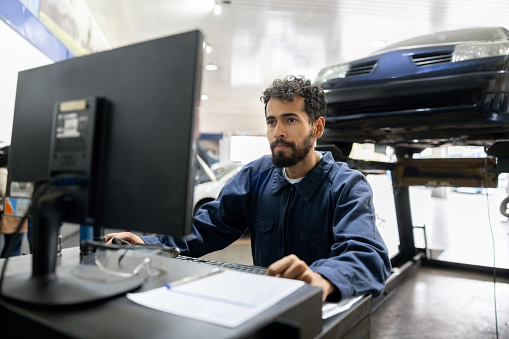 Latin American mechanic using a computer while working at a car garage