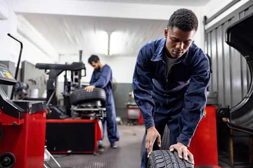 African American mechanic working at an auto repair shop fixing a flat tire - vehicle breakdown concepts