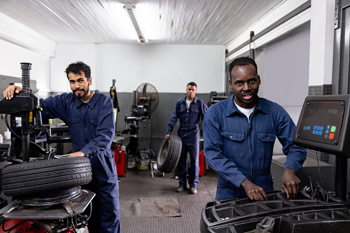 Happy group of mechanics working at a car garage fixing tires and looking at the camera smiling