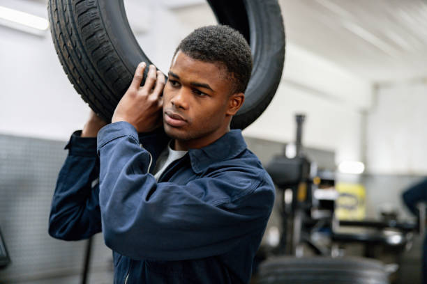 istock Mechanic working at a car garage carrying a tire 1831625996