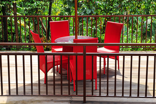 Garden gazebo with a glass table and red woven chairs with a trellis fence and umbrella