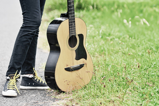 acoustic guitar and feet with shoes standing on green grass