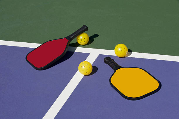 Pickleball - colorful paddles, ball and court Image of two pickleball paddles with three pickleballs on a colorful pickleball court. pickleball stock pictures, royalty-free photos & images